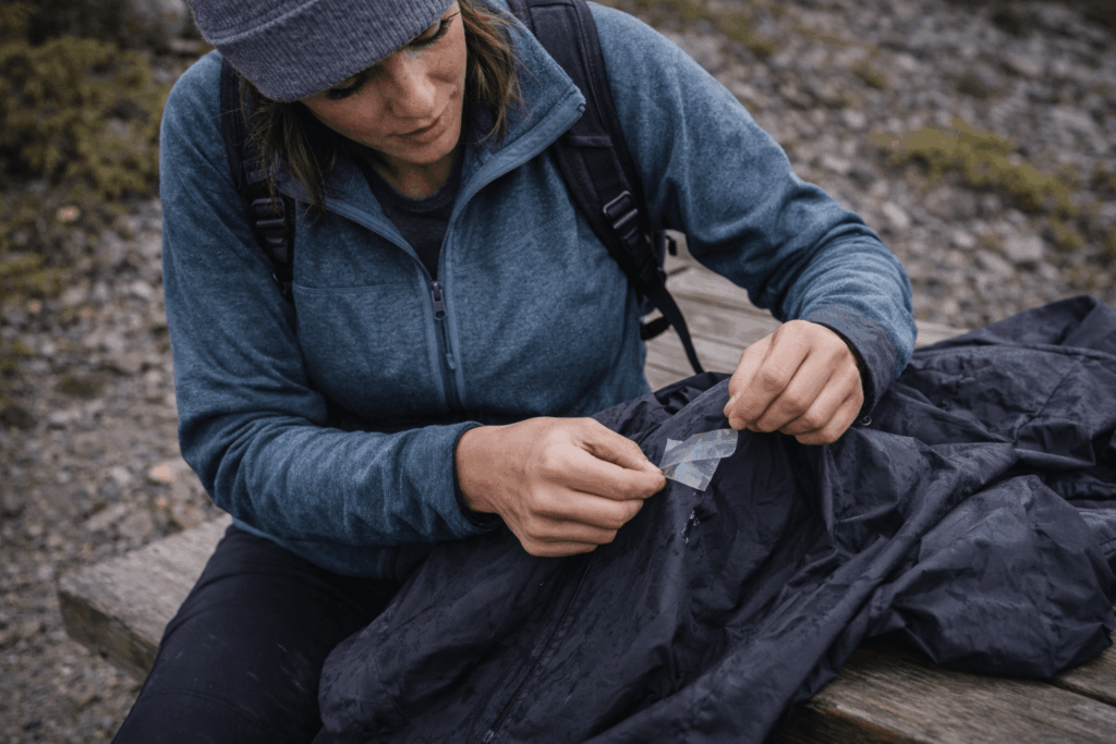 Wanderin klebt kleines Loch in Regenjacke mit Reparaturflicken
