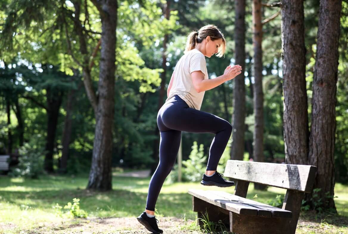 Outdoor Fitness: Frau macht Step-ups auf einer Parkbank im Wald – funktionelles Einbein-Training
