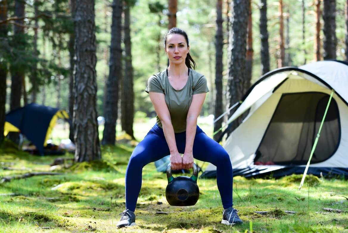 Frau macht Goblet Squat mit HQ Germany Kettlebell auf einem Campingplatz im Wald