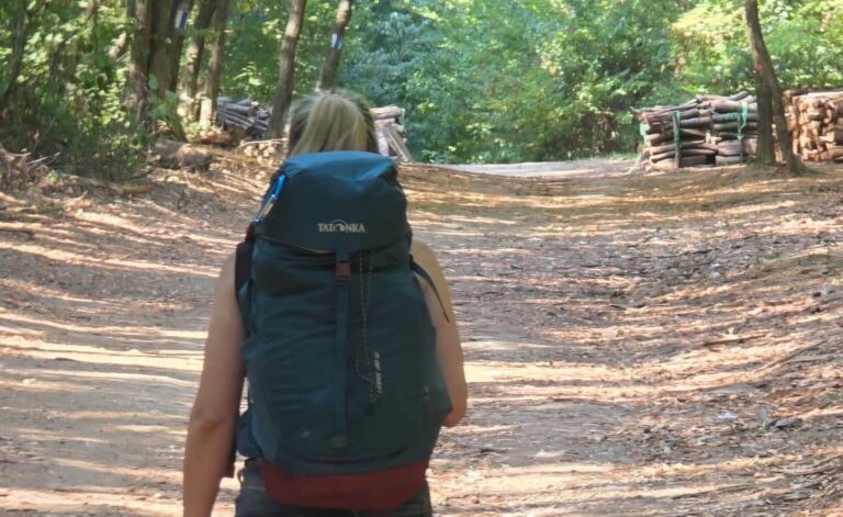 Frau trägt einen beladenen Trekkingrucksack auf einem Waldweg